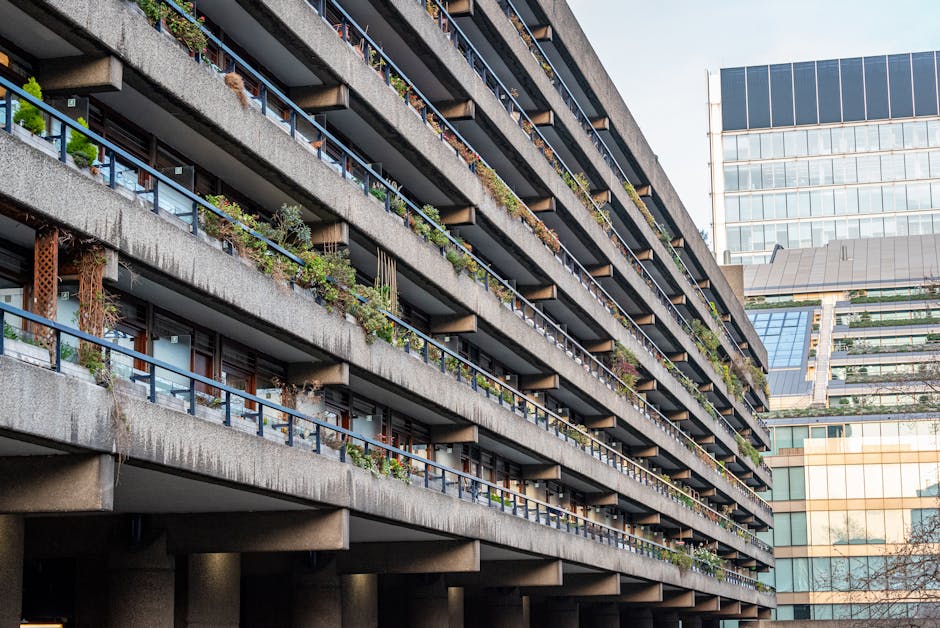 A multi-storey residential building with outdoor balconies featuring various potted plants and greenery, including small shrubs and flowering plants. The building's concrete structure shows horizontal